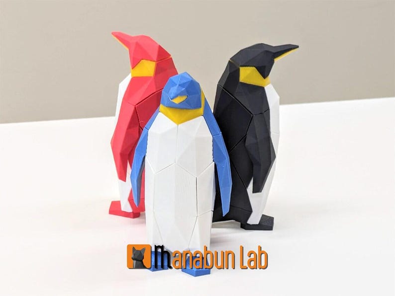 May include: Three origami penguins, one red, one black, and one white with blue wings. The penguins are standing on a white surface.