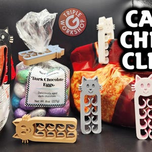 May include: A set of 3D printed cat chip clips in various colors, including black, gray, pink, and beige. The clips are shaped like cats with a smiling face and have a series of interlocking loops to secure the bag.