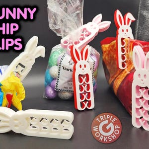 Puede incluir: Tres clips para patatas fritas en forma de conejo blanco, un clip para patatas fritas en forma de conejo rosa y un clip para patatas fritas en forma de conejo rojo. Los clips para patatas fritas en forma de conejo tienen forma de conejos con una fila de círculos en sus cuerpos. Los clips para patatas fritas en forma de conejo están sobre una mesa con una bolsa de chispas de chocolate y una bolsa de patatas fritas.