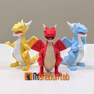 May include: Three origami dragons, one yellow, one red, and one blue, standing on a white surface. The dragons are all facing forward with their mouths open.