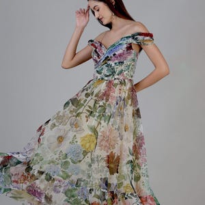 May include: Off-the-shoulder floral print dress with a flowing skirt. The dress features a variety of colorful flowers in shades of pink, purple, yellow, and green against a cream background. The dress has a fitted bodice and a ruffled hemline.