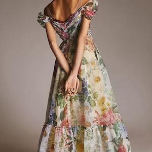 May include: A floral print maxi dress with an off-the-shoulder neckline. The dress features a variety of colorful flowers, including pink, yellow, and purple, on a cream-colored background. The dress has a ruffled hem and sheer straps.