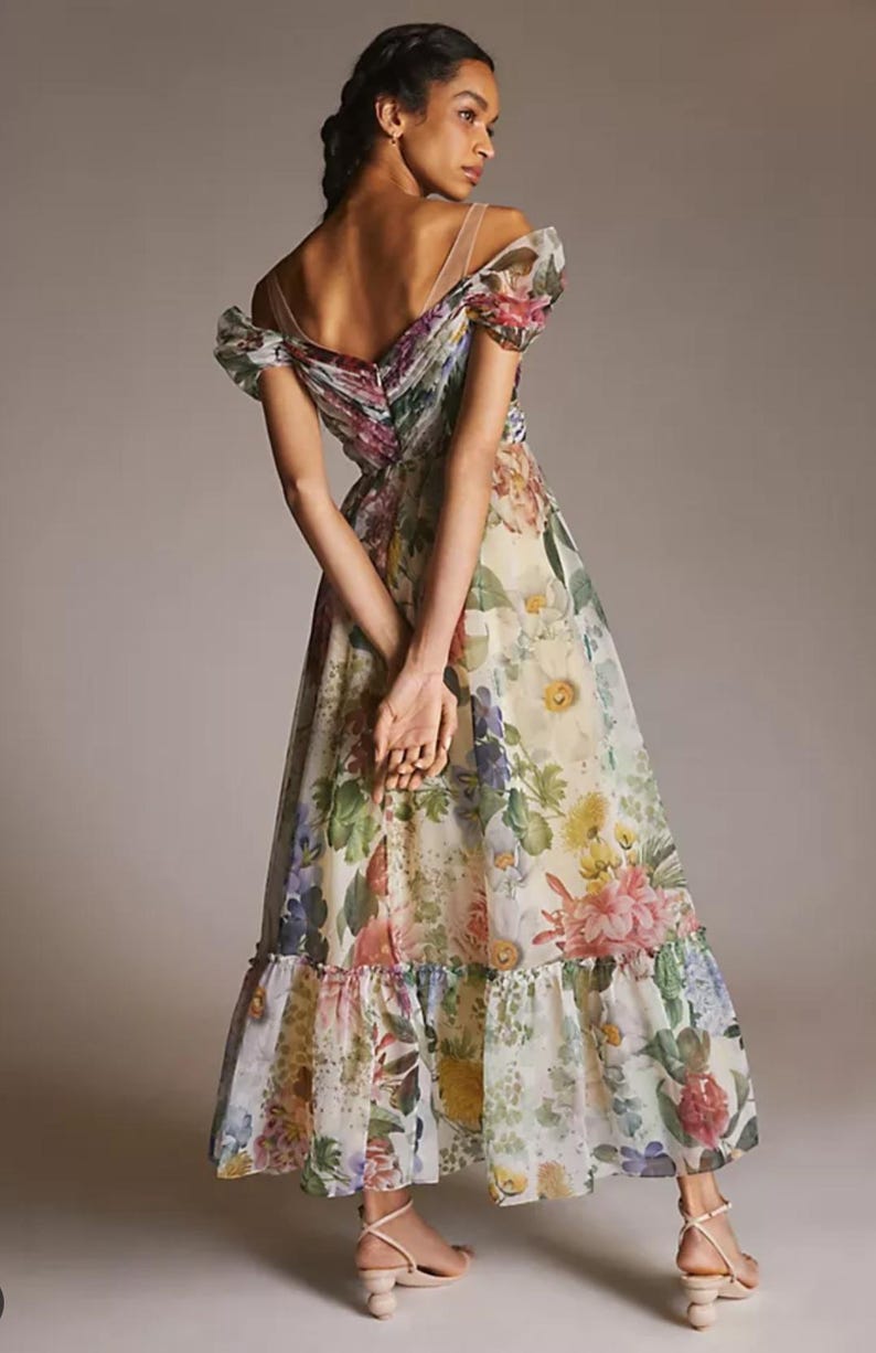 May include: A floral print maxi dress with an off-the-shoulder neckline. The dress features a variety of colorful flowers, including pink, yellow, and purple, on a cream-colored background. The dress has a ruffled hem and sheer straps.