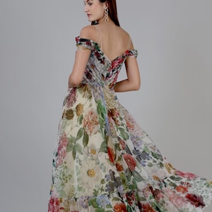 May include: A floral print off-the-shoulder dress with a flowing skirt. The dress features a variety of flowers in shades of red, pink, yellow, and green on a white background. The dress has a low back and sheer straps.