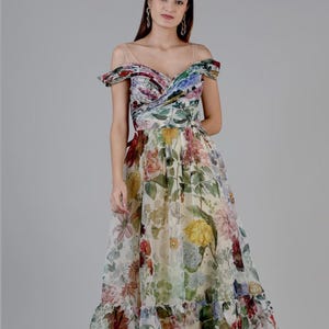 May include: A floral print maxi dress with an off-the-shoulder neckline. The dress features a variety of colorful flowers, including red, yellow, and purple blooms, set against a cream background. The dress has a flowing skirt and a ruffled hem.