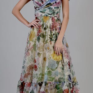 May include: A floral print off-the-shoulder dress with a sweetheart neckline. The dress features a variety of colorful flowers, including yellow, pink, and blue, on a cream-colored background. The dress has a flowing skirt and a ruffled hem.