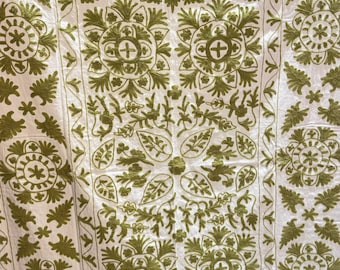 May include: White textile with intricate olive green embroidery. The design features floral and geometric patterns, including stylized flowers, leaves, and geometric shapes. The embroidery is detailed and covers the entire surface, creating a textured appearance.