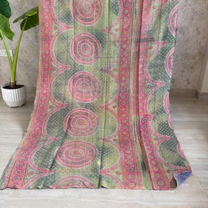 May include: A rectangular textile throw featuring a repeating pattern of large pink and green circular motifs. The fabric displays intricate geometric and floral-inspired details throughout, with visible running stitch textures across the surface.