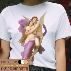 Könnte beinhalten: Weißes T-Shirt mit einem klassischen Gemälde von zwei sich umarmenden Figuren, mit Engelsflügeln und lila Draperien. Das Shirt hat den Text "MORE COLORS" und "100% ORGANIC COTTON" in Gold.