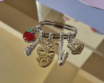 May include: A silver key chain with multiple charms, including a red apple, a microphone, a mask, a saxophone, and a tiger head.