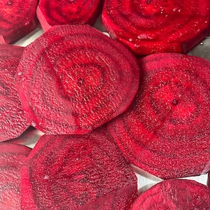 May include: Close-up of sliced red beets, showcasing their vibrant color and textured surfaces. The circular slices reveal concentric patterns, highlighting the natural beauty of the vegetable. A healthy food item.