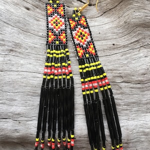 May include: A pair of long, black beaded earrings with a geometric pattern in red, yellow, and white. The earrings have a fringe of black beads.