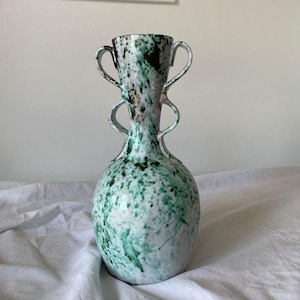 May include: A green and white ceramic vase with black speckles and two handles. The vase has a rounded body and a narrow neck.