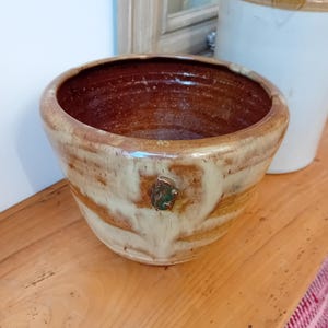 Peut inclure: Un bol en céramique brun et blanc avec un accent vert et brun. Le bol a un bord large et un fond arrondi.
