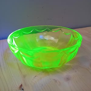 May include: A neon green glass bowl with a scalloped rim and leaf-like designs. The bowl is transparent, allowing light to pass through, and sits on a wooden surface. The bowl's vibrant color makes it a striking decorative piece.