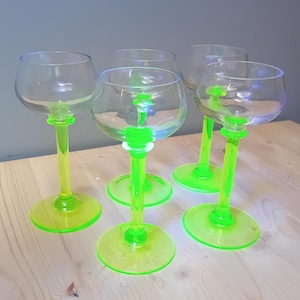 May include: Set of five clear glass wine glasses with neon green stems and bases. The glasses have a rounded bowl shape and a slender stem. The bases are circular, and the stems are a vibrant, eye-catching green.