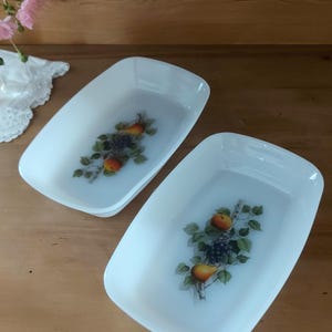 Könnte beinhalten: Zwei weiße rechteckige Backformen mit einem Fruchtdesign. Das Design zeigt Birnen, Äpfel und Trauben an einem Weinstock.
