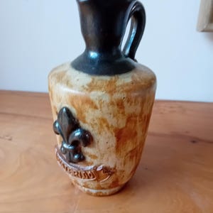 May include: A brown and black ceramic pitcher with a fleur-de-lis design and the word "Wurzburg" on the side.