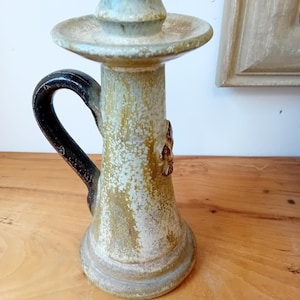 Peut inclure: Un chandelier en céramique avec une poignée brune et un glaçage blanc et vert. Le chandelier a un motif floral sur le côté.