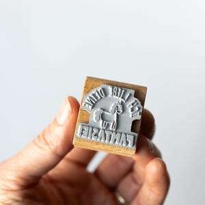 May include: A wooden stamp with a gray rubber stamp face. The stamp reads "The Divine Fantasie" around a graphic of a unicorn. The stamp is held in a person's hand against a white background.