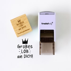 Op de afbeelding: Een houten stempel met de tekst "Großes - LOB - an DICH!" en een kroonsymbool, naast een witte en zwarte stempel met de merknaam "trodat edy". De houten stempel heeft ook de tekst "kreativpünktchen".