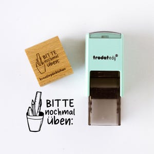 Könnte beinhalten: Ein Holzstempel und ein mintgrüner Selbstfärbestempel. Der Holzstempel trägt den Text "BITTE nochmal üben: kreativpünktchen" und eine Zeichnung von Bleistiften und einem Lineal in einem Becher. Der Selbstfärbestempel trägt den Text "trodat edy".