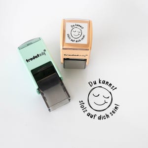 Può includere: Due timbri con la scritta "Du kannst stolz auf dich sein!" e una faccina sorridente. Un timbro è verde menta, l'altro è beige. Il testo è nero. Il marchio "trodatedy" è stampato sui timbri.