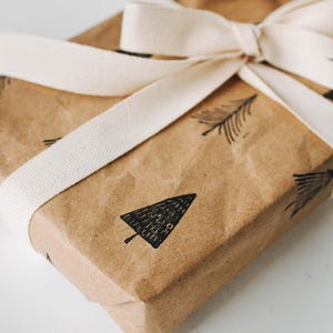 Peut inclure: Un sac cadeau en papier brun avec un ruban blanc nou&eacute; en un n&oelig;ud. Le sac est d&eacute;cor&eacute; de tampons d'arbres noirs et blancs.