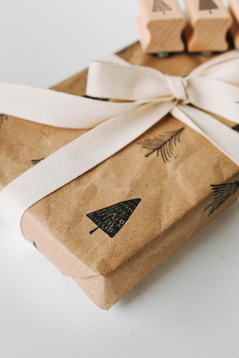 Peut inclure: Un sac cadeau en papier brun avec un ruban blanc nou&eacute; en un n&oelig;ud. Le sac est d&eacute;cor&eacute; de tampons d'arbres noirs et blancs.