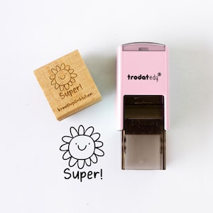 May include: A wooden stamp and a pink self-inking stamp with a smiling sunflower design and the word "Super!" in black. The wooden stamp also includes the text "kreativp&uuml;nktchen". The self-inking stamp has the brand name "trodatedy" in white.