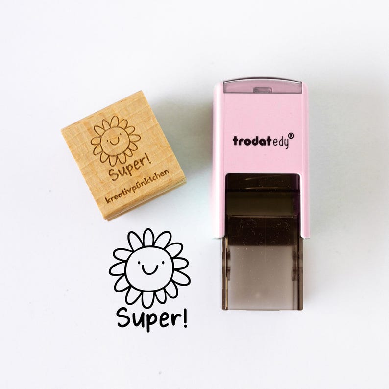 May include: A wooden stamp and a pink self-inking stamp with a smiling sunflower design and the word "Super!" in black. The wooden stamp also includes the text "kreativp&uuml;nktchen". The self-inking stamp has the brand name "trodatedy" in white.