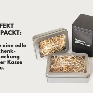 May include: Three silver gift boxes with clear lids. The boxes are filled with shredded paper and have the text "kreativ p&uuml;nktchen" printed on them. The text "PERFEKT VERPACKT: F&uuml;ge eine edle Geschenk-verpackung an der Kasse hinzu." is printed on the left side of the image.