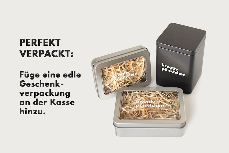 May include: Three silver gift boxes with clear lids. The boxes are filled with shredded paper and have the text "kreativ p&uuml;nktchen" printed on them. The text "PERFEKT VERPACKT: F&uuml;ge eine edle Geschenk-verpackung an der Kasse hinzu." is printed on the left side of the image.