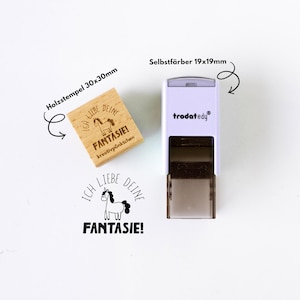 May include: A wooden stamp (30x30mm) and a self-inking stamp (19x19mm) with the text "ICH LIEBE DEINE FANTASIE!" and a unicorn illustration. The wooden stamp is light brown, and the self-inking stamp is white and gray.