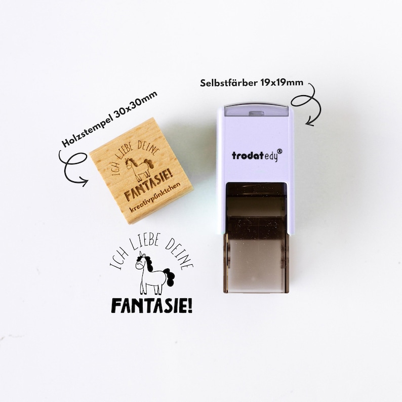 May include: A wooden stamp (30x30mm) and a self-inking stamp (19x19mm) with the text "ICH LIEBE DEINE FANTASIE!" and a unicorn illustration. The wooden stamp is light brown, and the self-inking stamp is white and gray.
