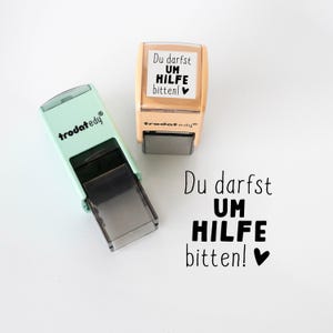 May include: Two self-inking stamps. One is mint green, the other is tan. Both have the text "Du darfst UM HILFE bitten!" in black. The mint green stamp has the brand name "trodat edy" in green. The tan stamp has the same brand name in black.