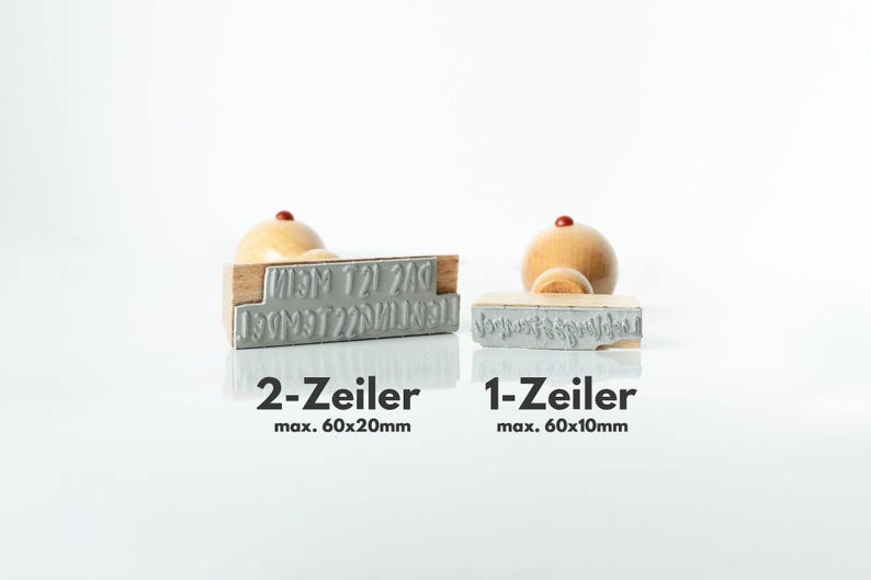 May include: Two wooden stamps with metal lettering, one larger and one smaller, with wooden handles. The larger stamp is labeled "2-Zeiler" and the smaller one is labeled "1-Zeiler". The text "max. 60x20mm" and "max. 60x10mm" is also visible.