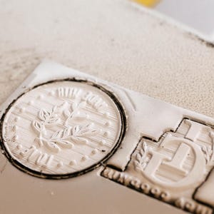May include: Close-up of a white rubber stamp with a floral design and the word "Made with Love" in a circle. The stamp is on a white surface.