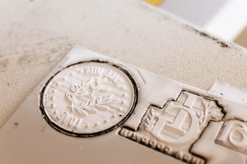 May include: Close-up of a white rubber stamp with a floral design and the word "Made with Love" in a circle. The stamp is on a white surface.