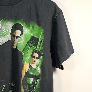 May include: A charcoal gray short-sleeve t-shirt featuring a graphic print of two figures wearing black sunglasses against a bright green background with lightning effects. The shirt has a crew neckline and a Changes brand label at the inner collar.