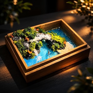 May include: A miniature diorama scene in a wooden box. The scene depicts a bridge over a waterfall and a body of water with a small figure. The landscape includes green and orange foliage, a sandy beach, and a blue water feature.