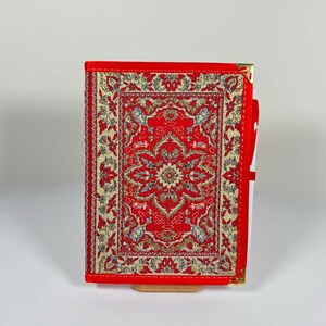 Könnte beinhalten: Ein rotes Notizbuch mit goldenen Mustern und einem goldenen Reißverschluss. Das Notizbuch hat einen roten und goldenen Musterbezug mit einem floralen Design.