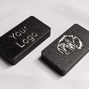 May include: Two black rectangular objects with a textured surface. One has the text "Your Logo" in white. The other features a white graphic design. These are likely promotional items or custom-made products.
