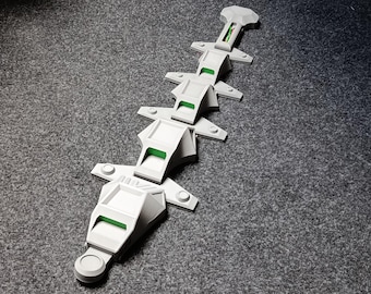 May include: A white, geometric object with green detailing, possibly a model or component, arranged in a linear pattern. The object's segments are connected. The background is a textured grey surface.