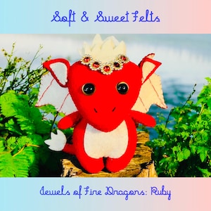 May include: Red felt dragon with white wings and a crown of white felt and red jewels. The dragon is sitting on a wooden stump. The text "Jewels of Fire Dragons: Ruby" is below the dragon.