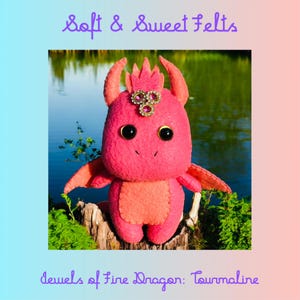May include: A pink felt dragon with a jeweled crown, called "Jewels of Fire Dragon: Tourmaline". The dragon is sitting on a tree stump in front of a body of water.