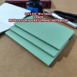 May include: Three mint green pocket travel notebook refills, each measuring 9 x 14cm. The image also shows a white notebook, a bottle of ink, and a pen. The text on the image reads "REFILLS FOR POCKET TRAVEL NOTEBOOK".