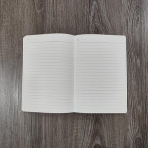 以下が含まれることがあります： 水平の黒い罫線と各ページの上部に小さな日付欄がある白いページを備えた開いたノートブック。ノートブックは平らに置かれており、書き込みの準備が整った2枚の空白ページが表示され、すっきりとシンプルなレイアウトデザインになっています。