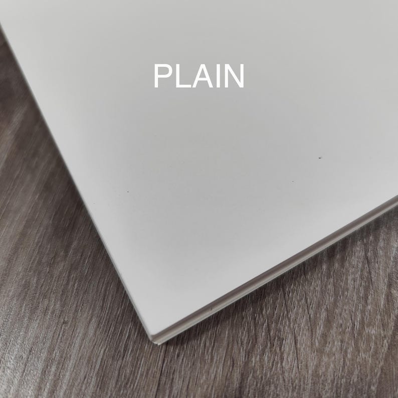 May include: A white, rectangular object with the word "PLAIN" printed in the centre. The object is angled, showing its edge, and is set against a wooden surface.
