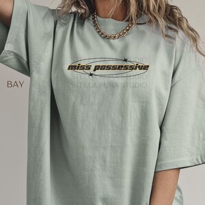 A light green t-shirt with the text 'miss possessive' in black and orange lettering with a black star design around the text.